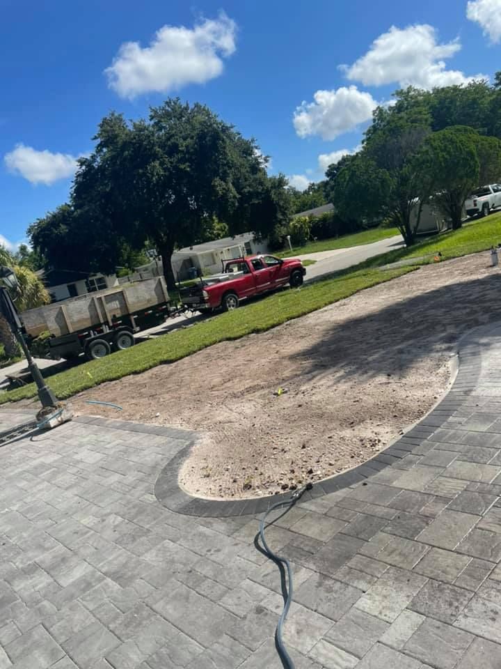 Paver driveway with a dirt area, a red truck, and a trailer on a sunny day.