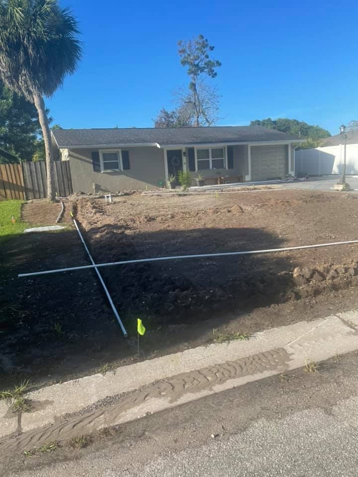 House with landscaping under construction, brown soil, white pipes, green grass, and blue sky.
