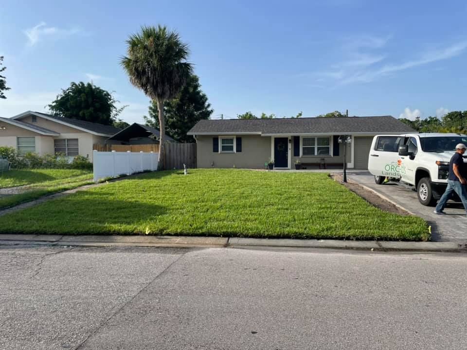 A ranch-style house with green lawn, white van, and person walking in front on a sunny day.