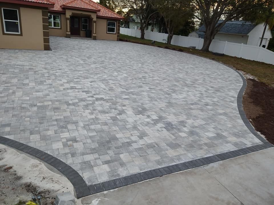 Paver driveway leading to a house with a curved dark border, gray and tan pavers.
