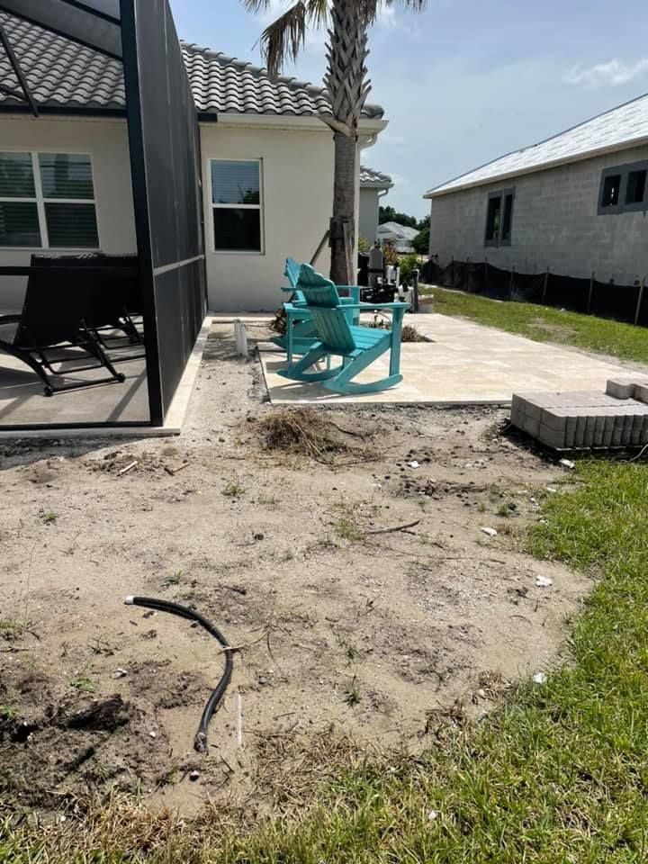 Backyard patio under construction with dirt, pavers, and blue chairs.