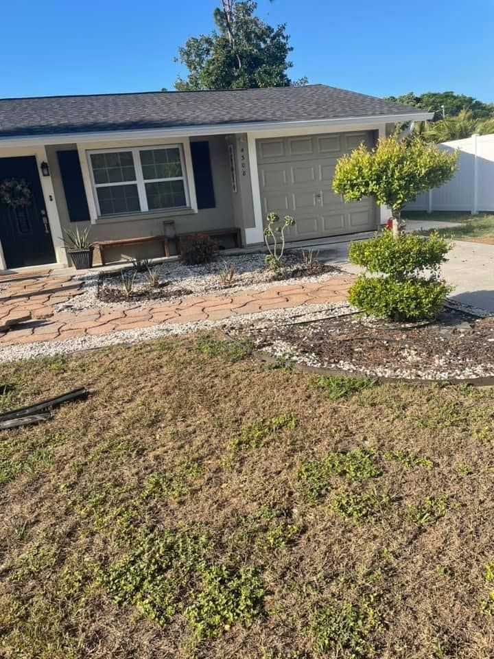 Tan house with gray garage door, brick walkway, and a small, manicured tree.