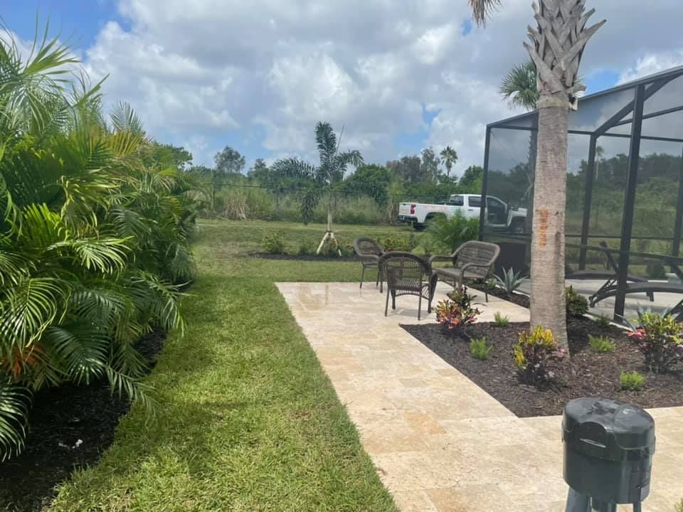 Backyard with a stone path, patio furniture, and lush greenery under a cloudy sky.