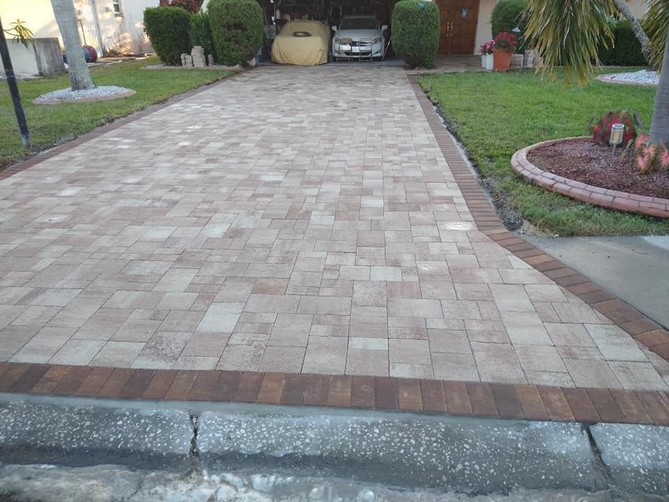 Brick paver driveway leading to a house, edged with darker bricks, green lawn on either side.