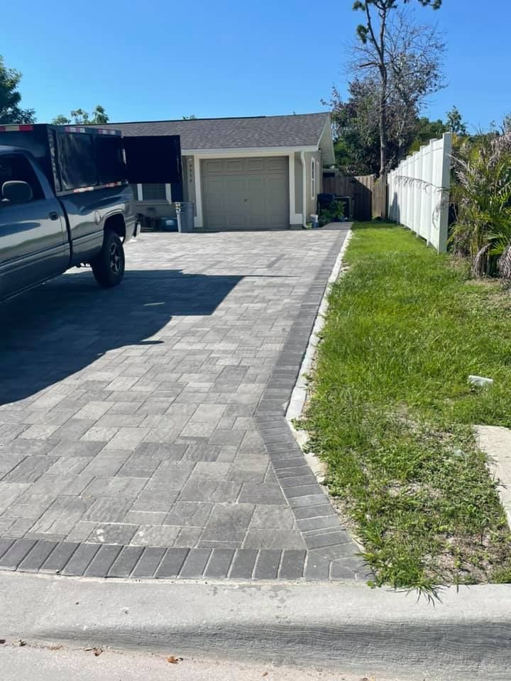 Paver driveway leading to a garage. A truck is parked on the left. Green grass borders the driveway.