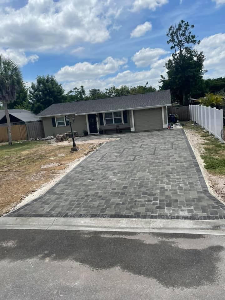 A house with a newly paved gray brick driveway under a partly cloudy sky.