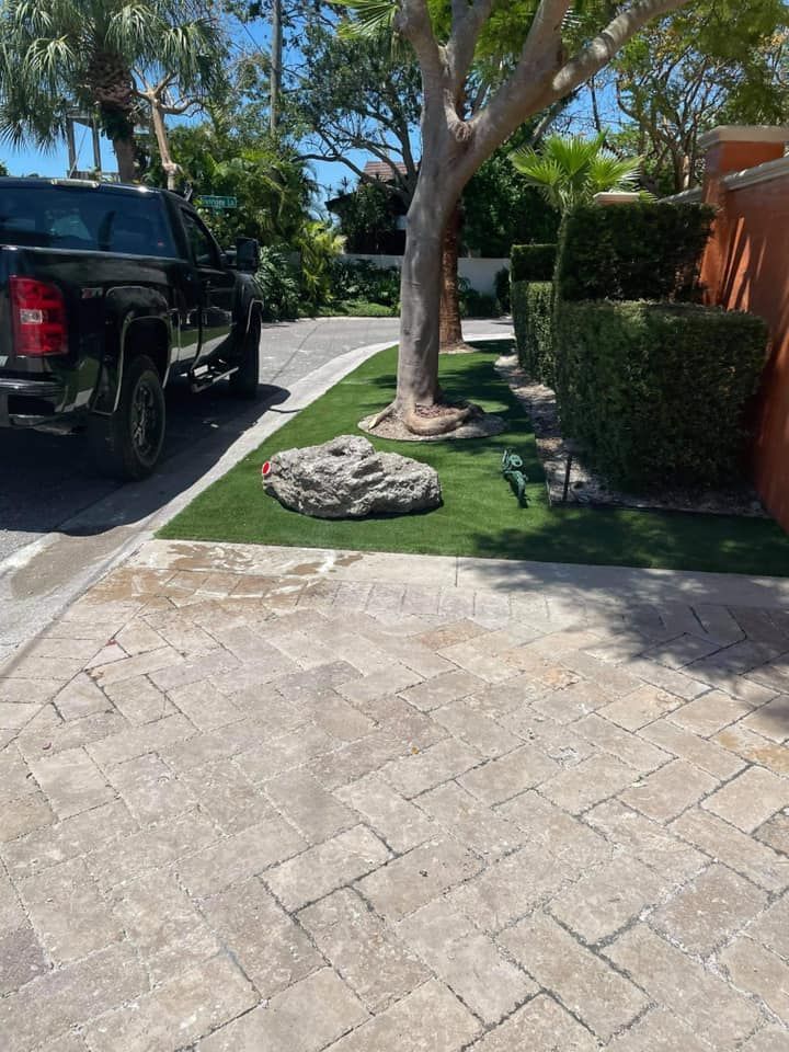 Black truck parked on a cobblestone driveway next to a small lawn with a large rock and a tree.