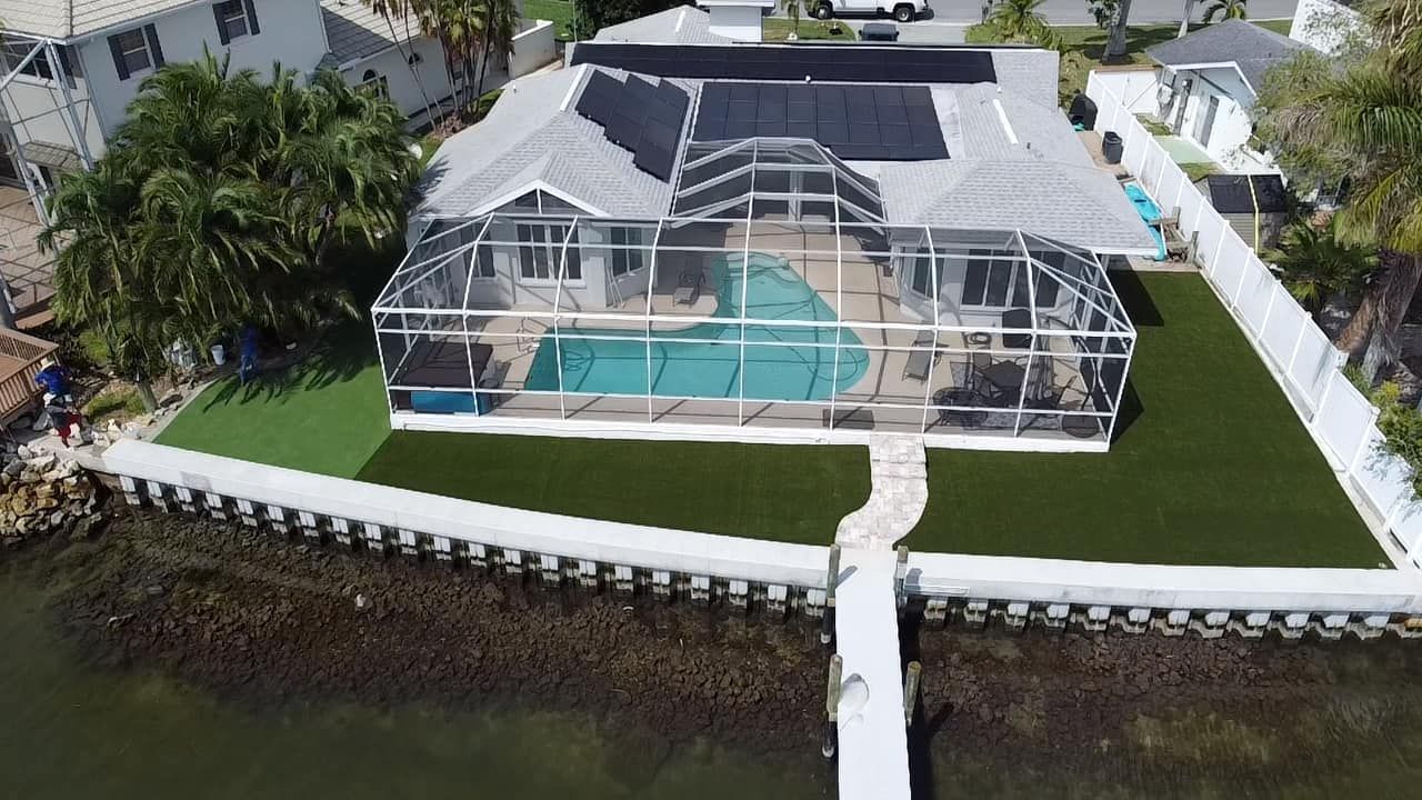 Aerial view of a waterfront house with a screened-in pool, dock, and landscaped yard.