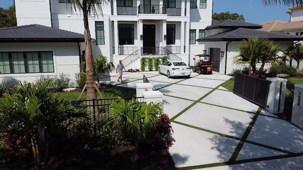 A white modern house with a large, geometric-patterned driveway featuring green turf strips, a white car, and a golf cart.
