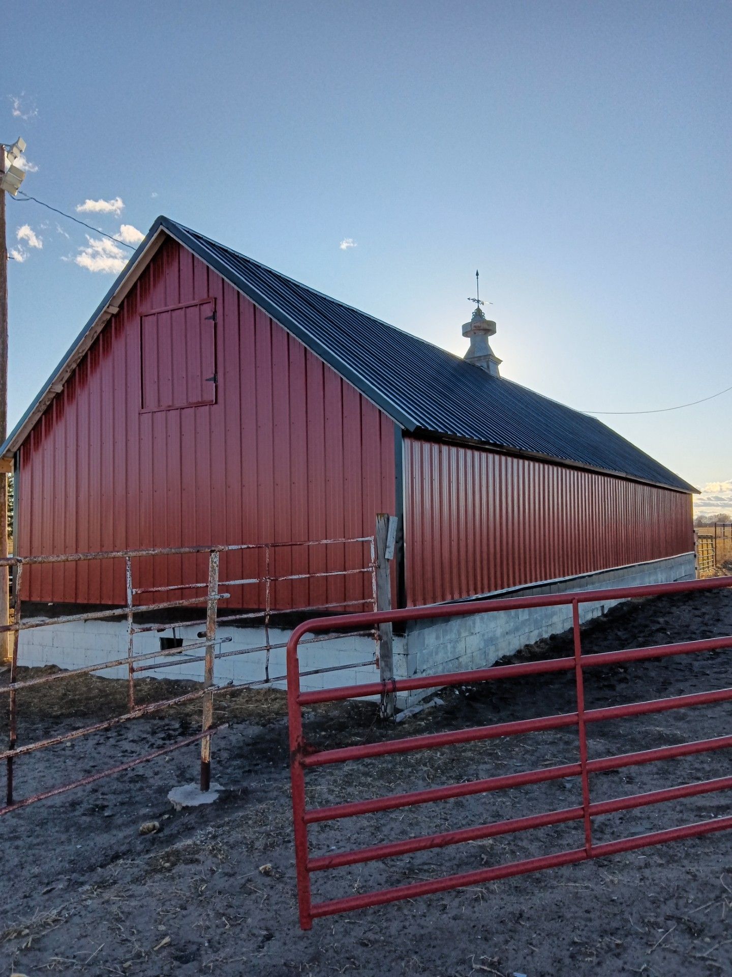 A red barn with a black roof is surrounded by a red fence.