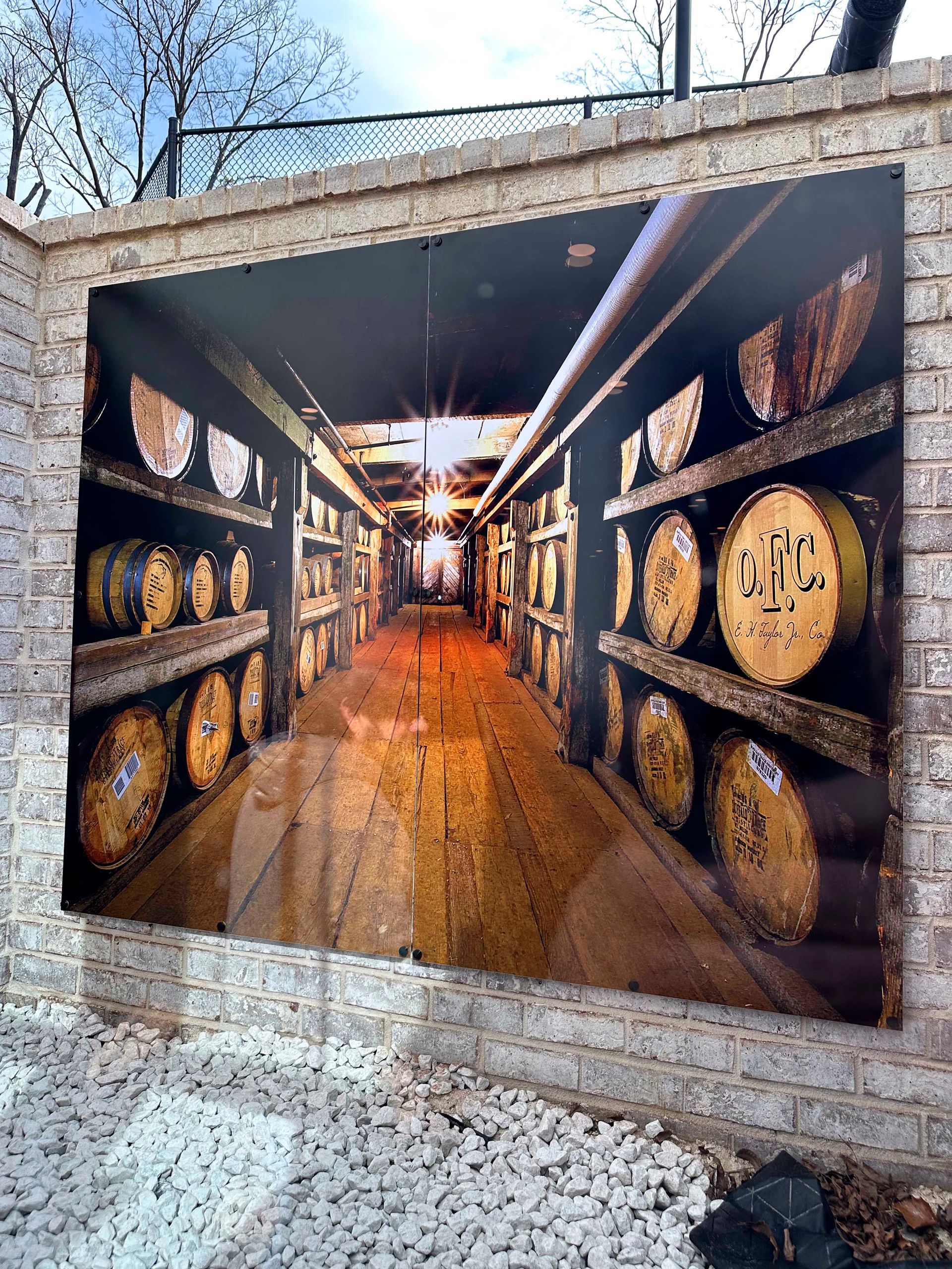 Photograph of a bourbon barrel aging warehouse interior, barrels stacked on shelves, bright light at the end of the aisle.