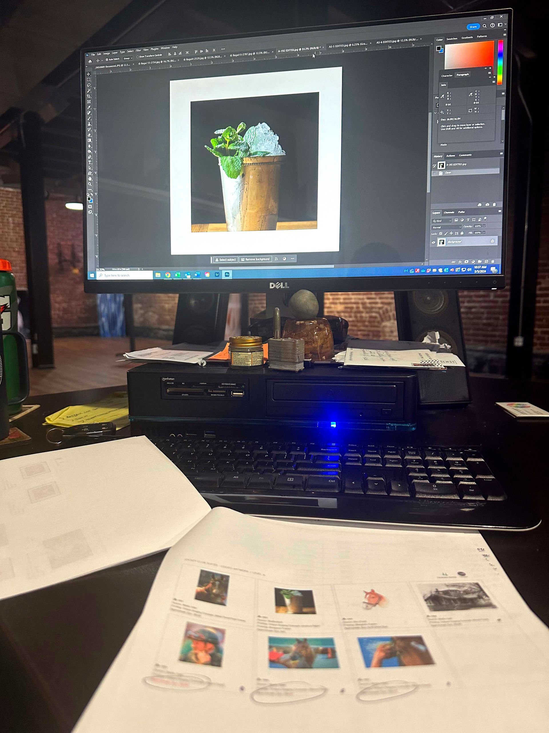 Computer screen showing an artwork with a vase of flowers, desk with keyboard, printed images and papers.