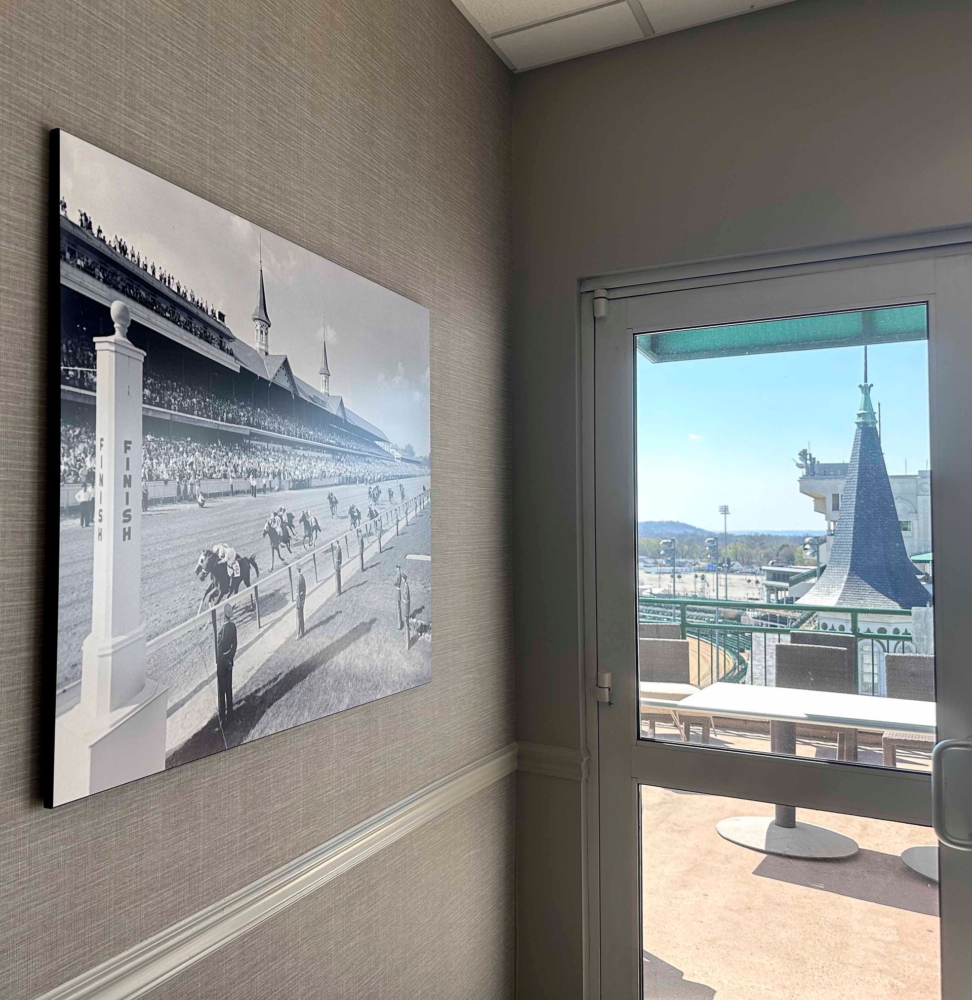 Black and white photo of a horse race on a wall. Door leads to a sunny outdoor space.