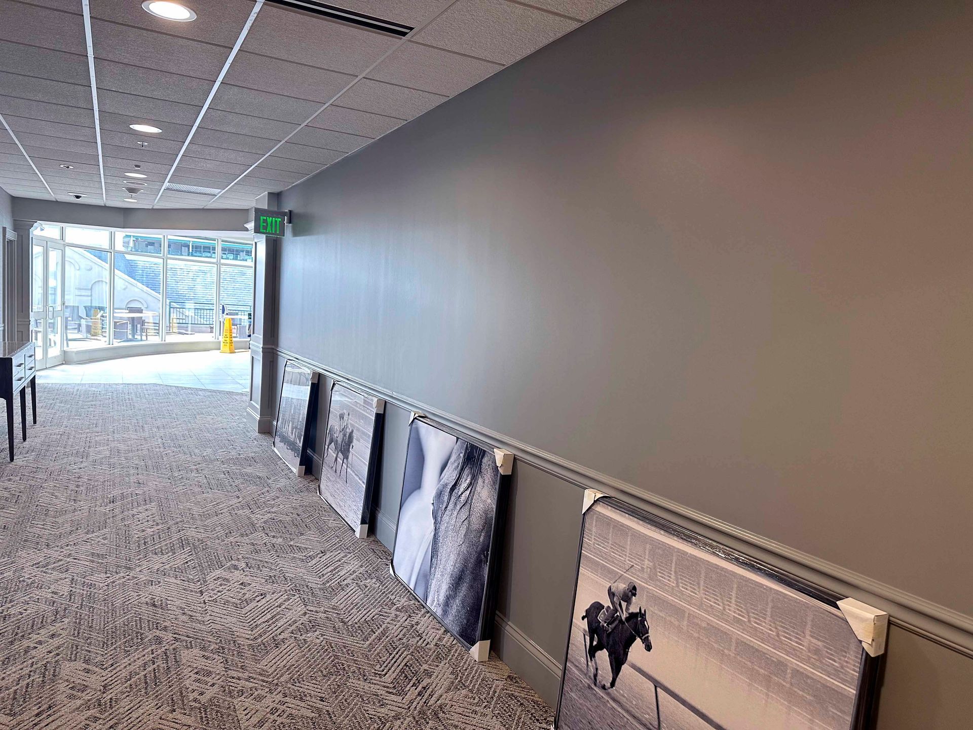 Hallway with neutral carpet, gray walls, and framed art. Bright light at the end leads to an outdoor view.