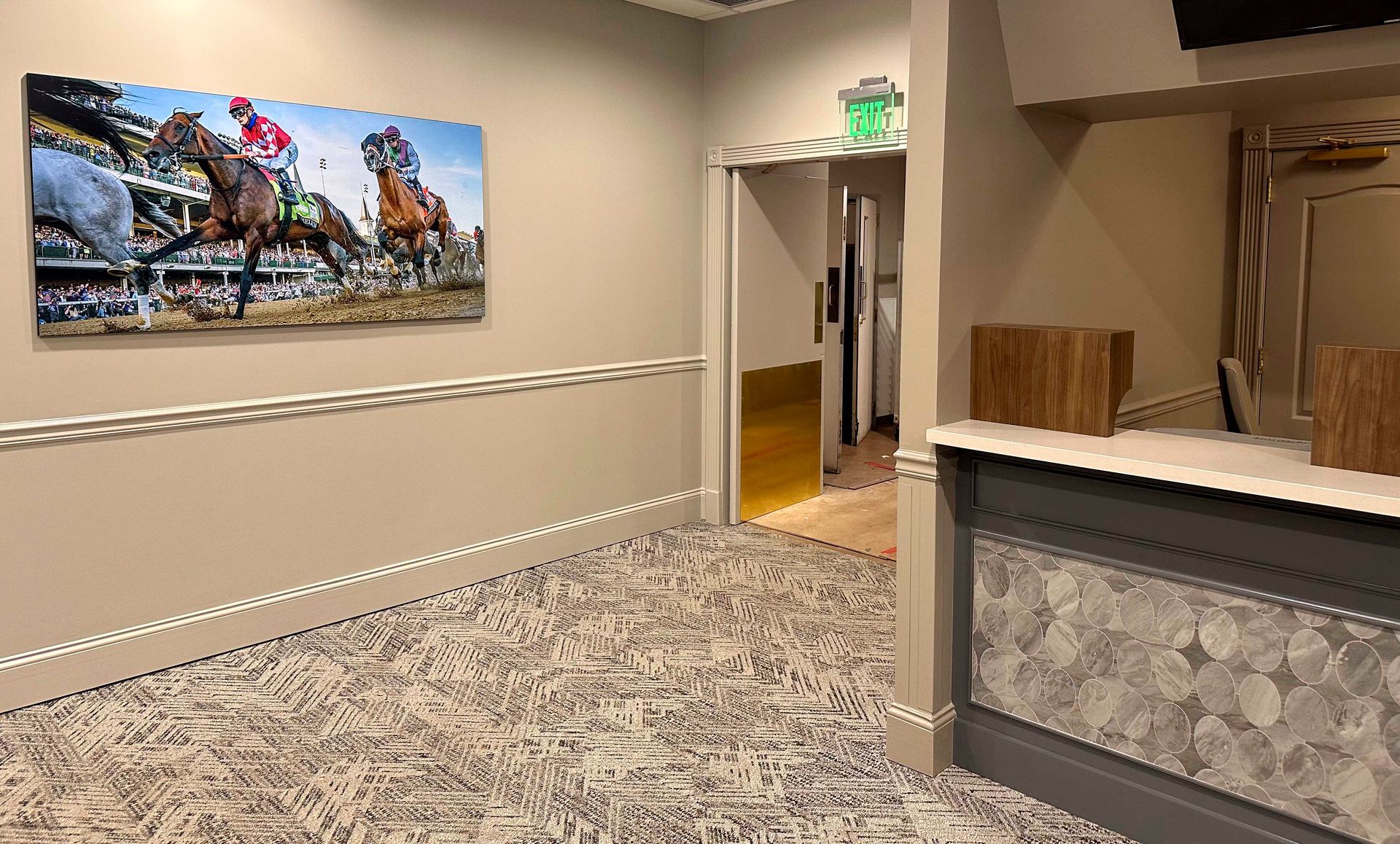 Hallway with horse racing art. Neutral colored walls, patterned flooring, and a doorway.