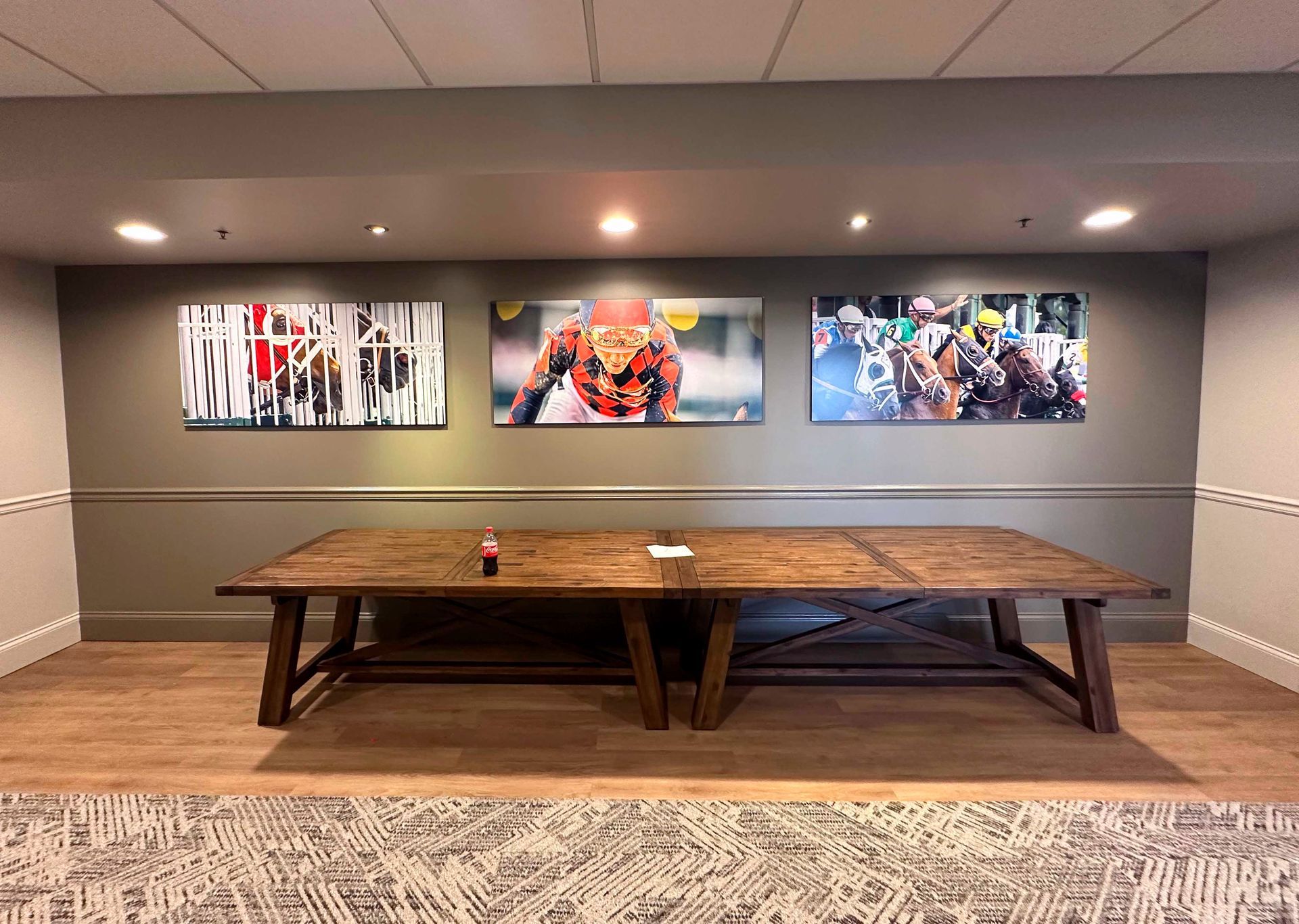 Three photos above a large wooden table in a room with a light wood floor and gray wall.
