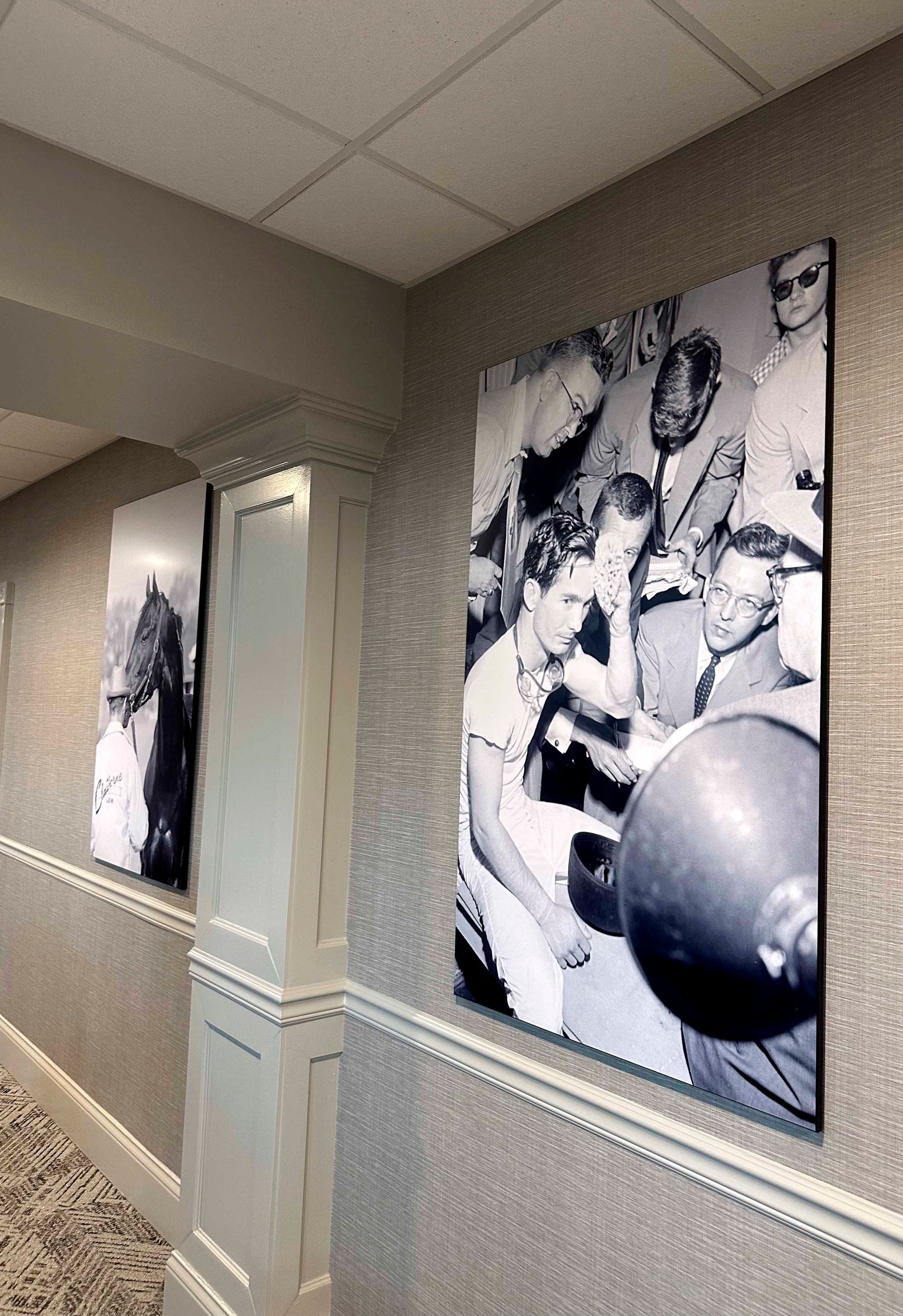 Hallway with large black and white photos. One shows a man lifting weights, the other, a horse.
