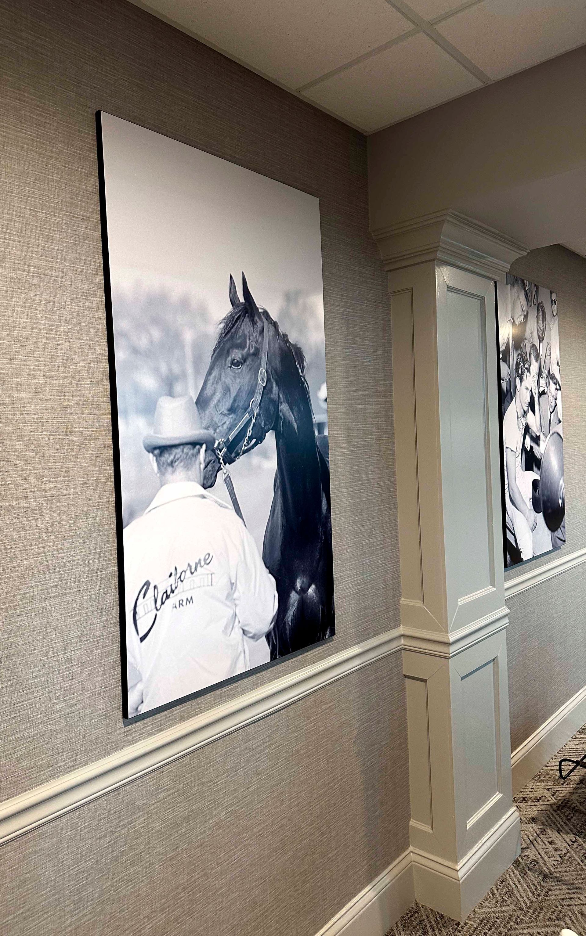 Black and white photo of a horse and handler; the horse is wearing a bridle and the handler is wearing a 