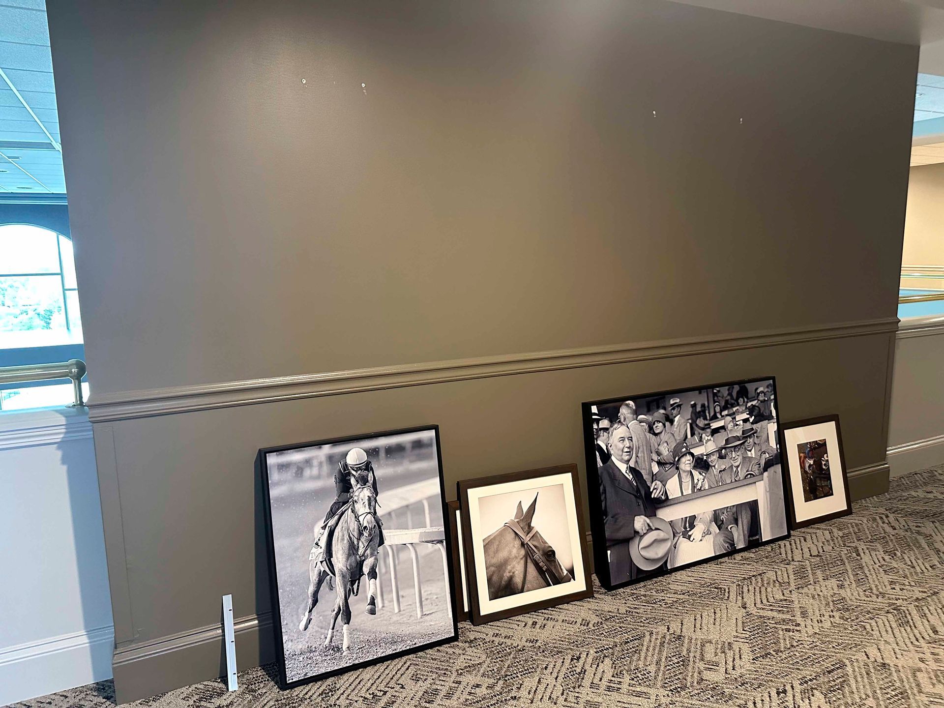Black and white horse racing photos leaning against a wall on carpet.