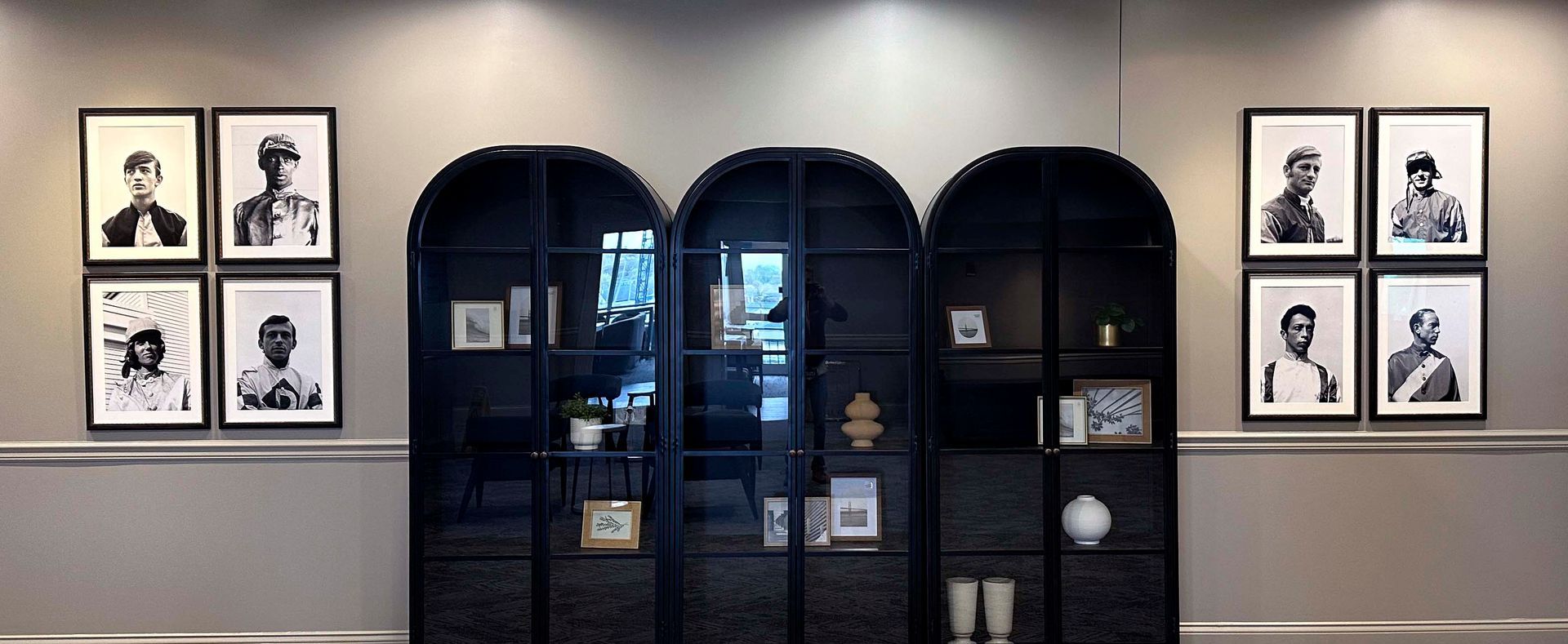 Wall with framed black and white portraits and a black cabinet with shelves.