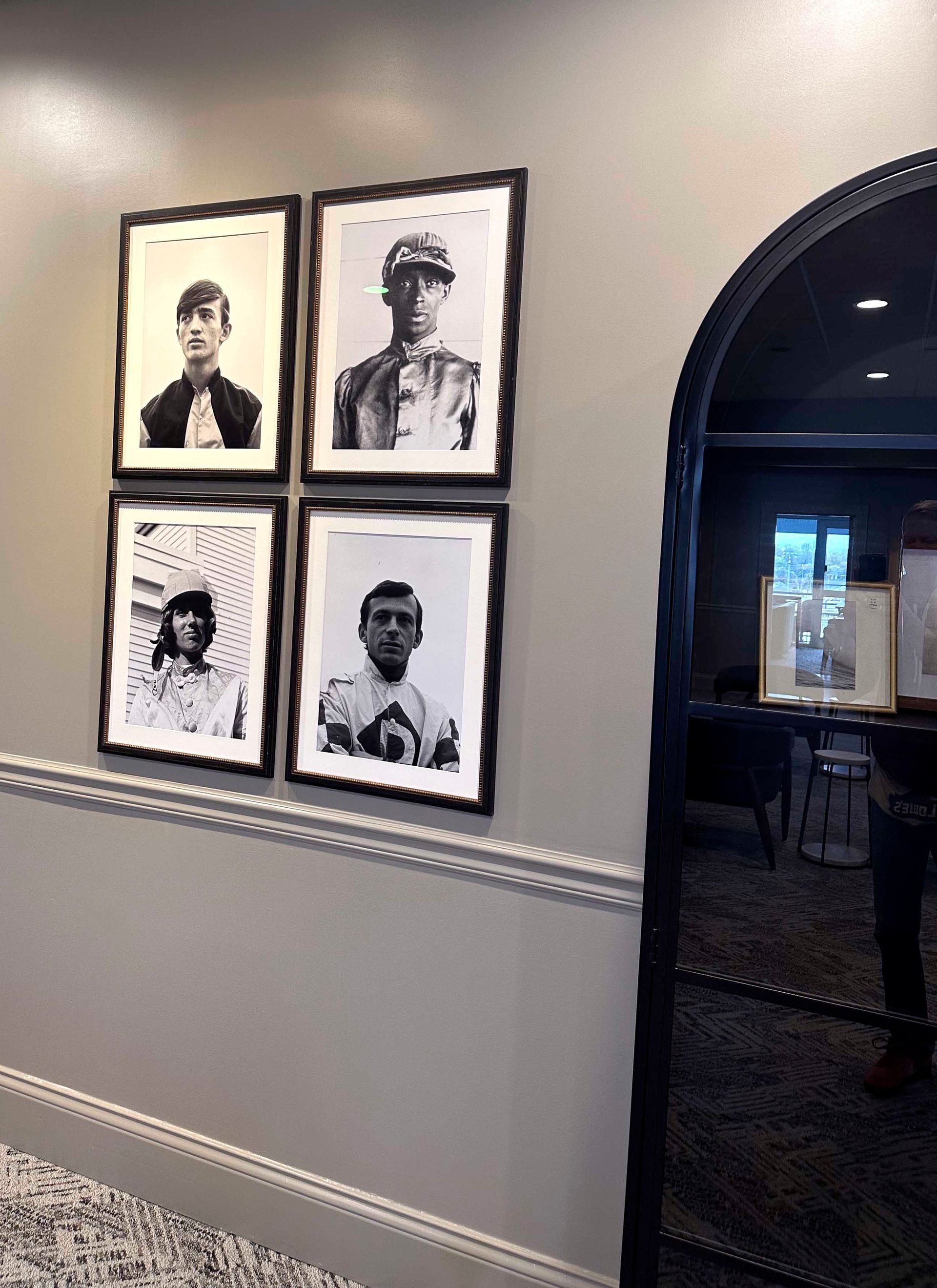 Four framed black and white portraits on a gray wall, near an arched doorway.