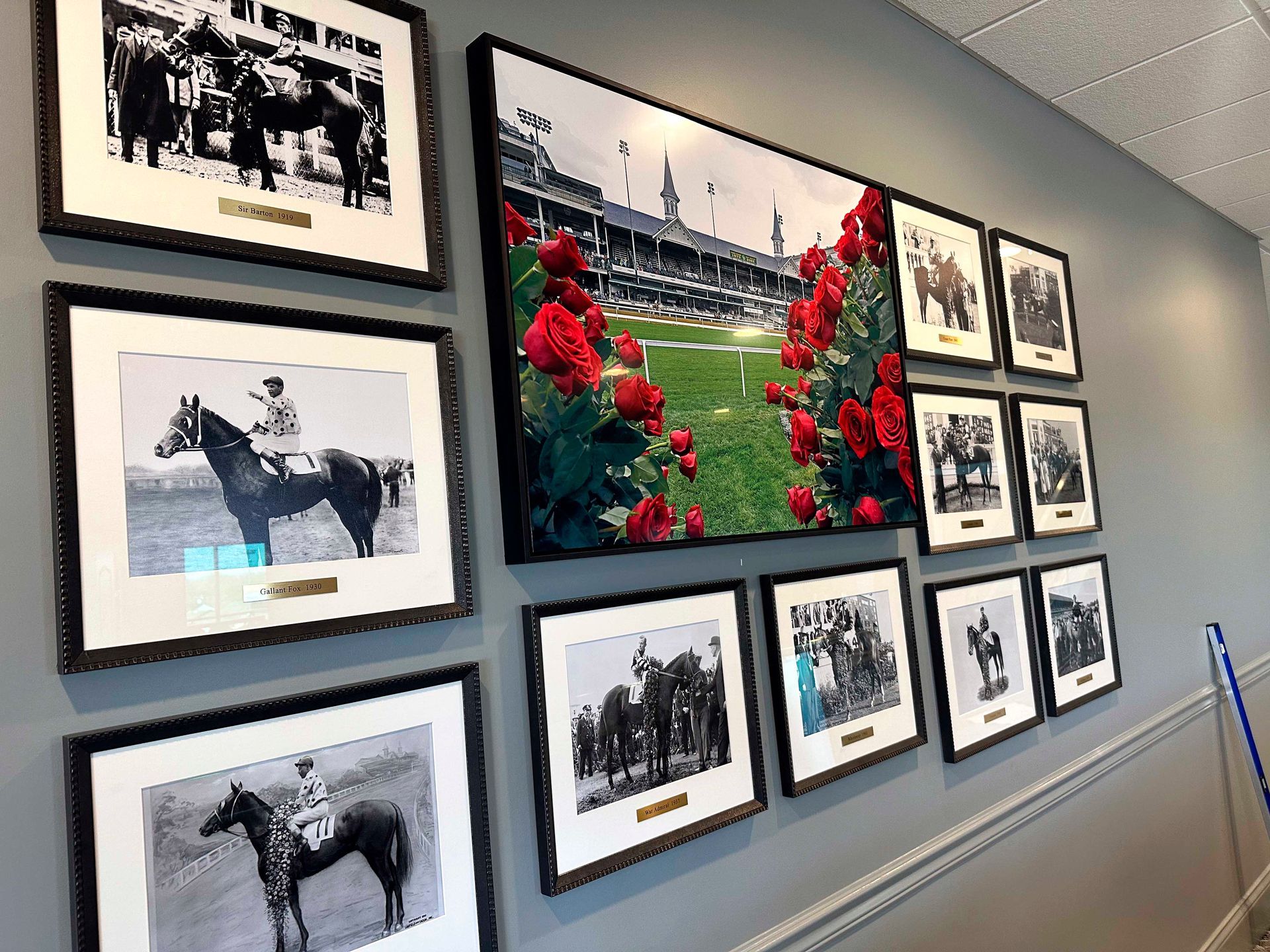 Wall display of framed horse racing photos and a color print of a racetrack with roses.