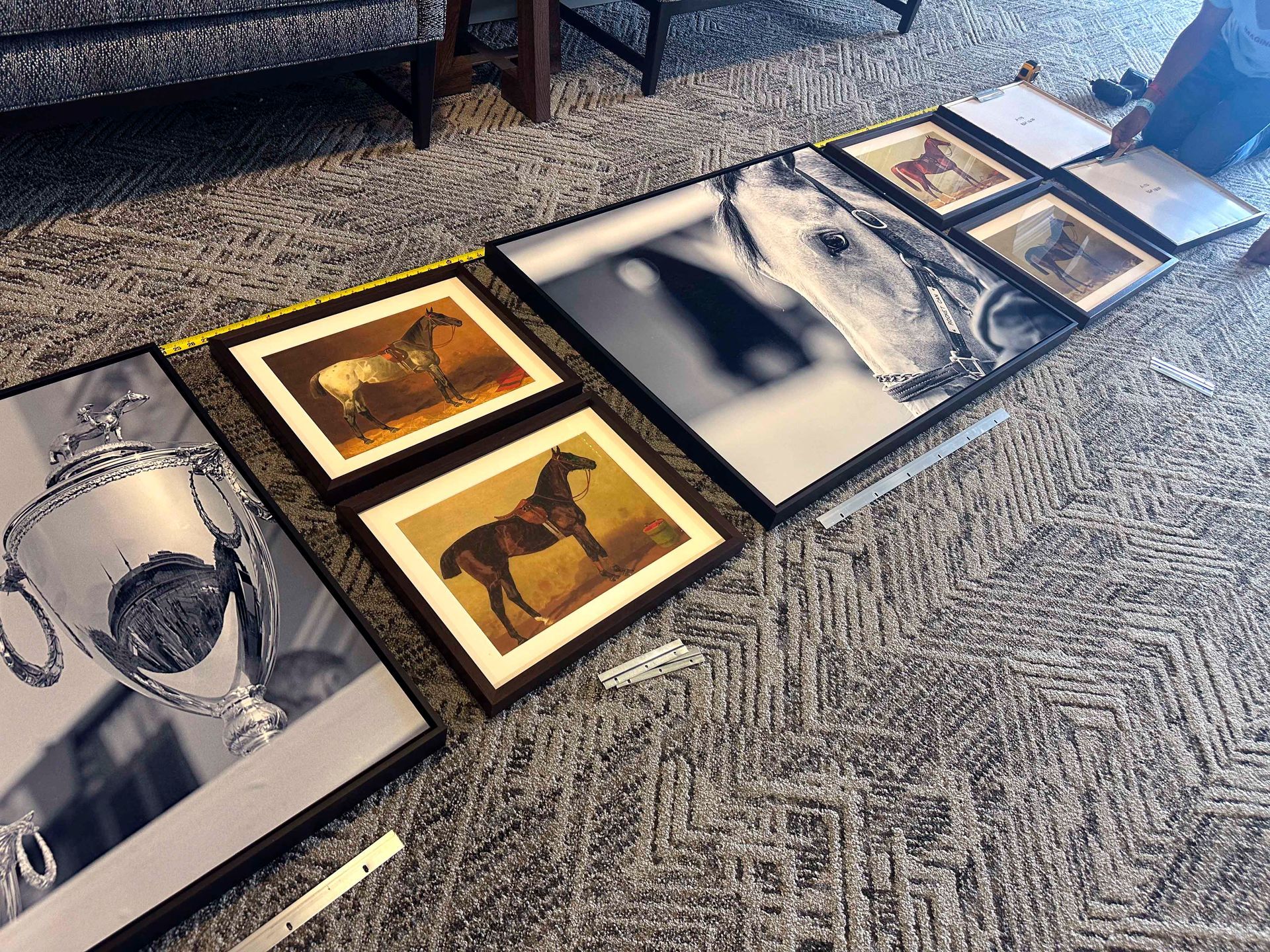 Horse-themed framed art laid out on carpet, including a trophy, paintings, and a close-up of a horse's face.