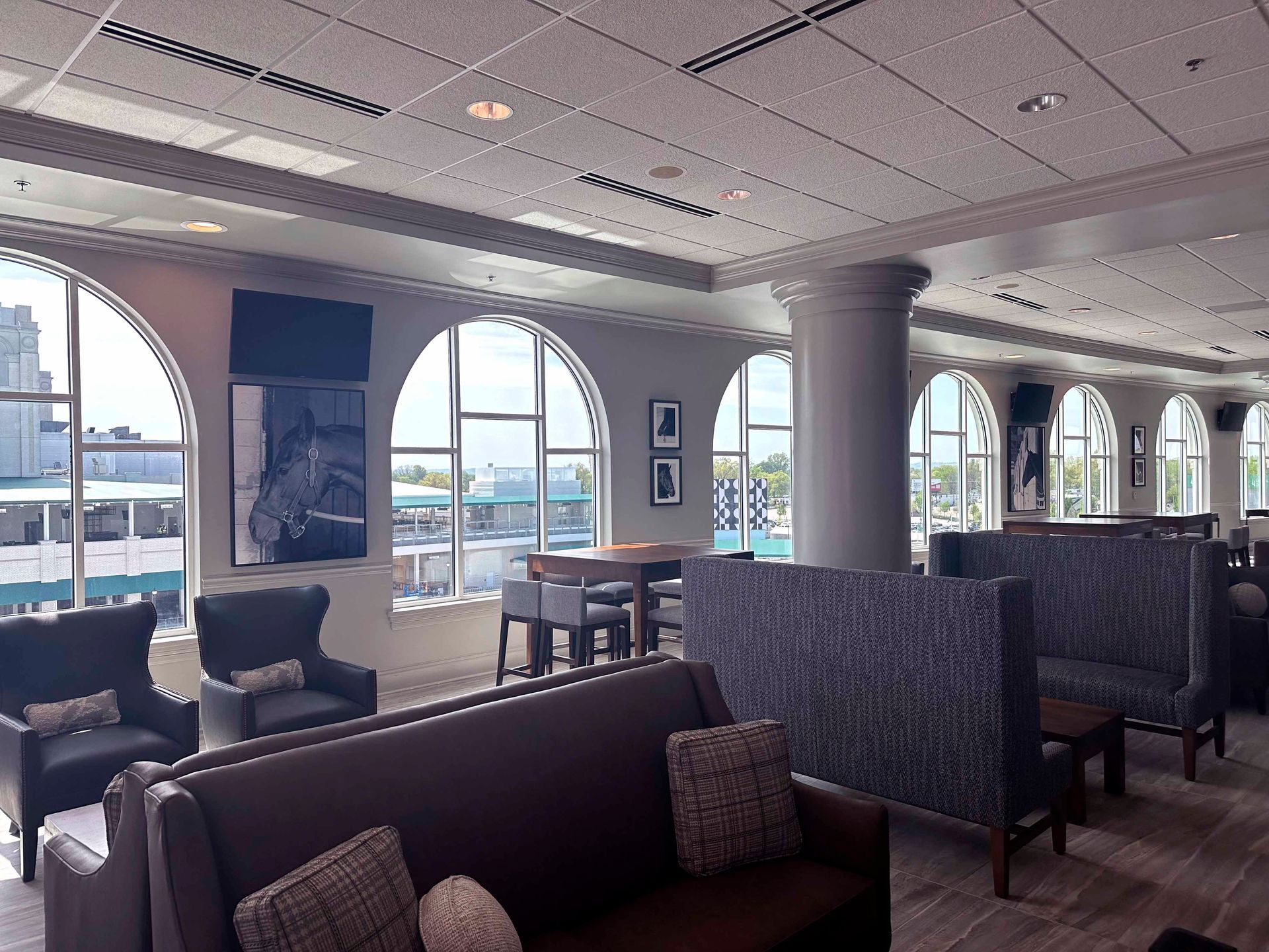 Lounge with arched windows overlooking a city. Sofas, armchairs, and tables are arranged for seating.