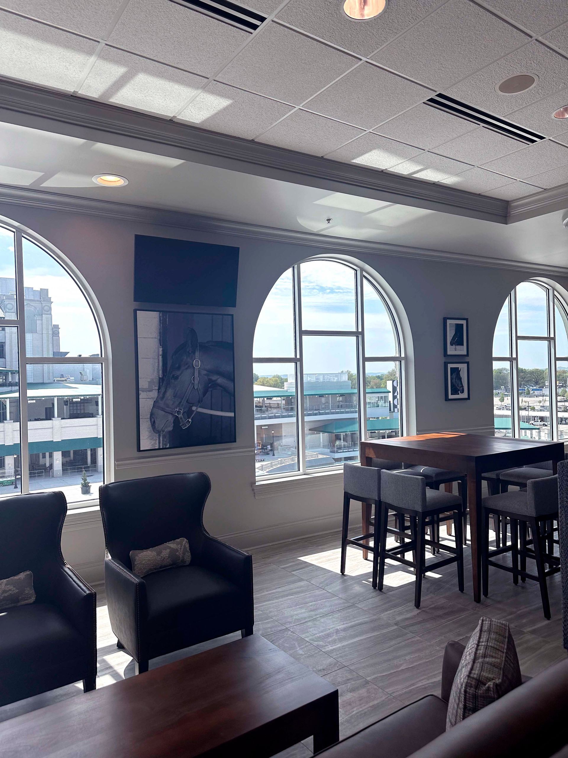 Lounge area with arched windows, city view, dark leather armchairs, a table with bar stools, artwork, and a TV.