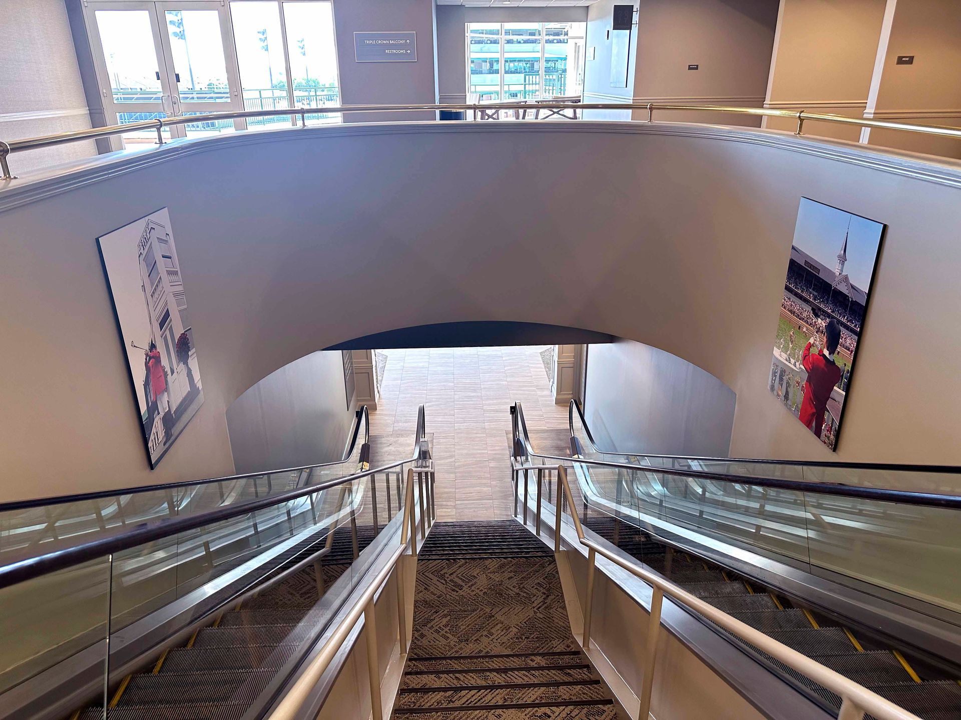 Escalators descend into an archway; framed artwork hangs on both sides.