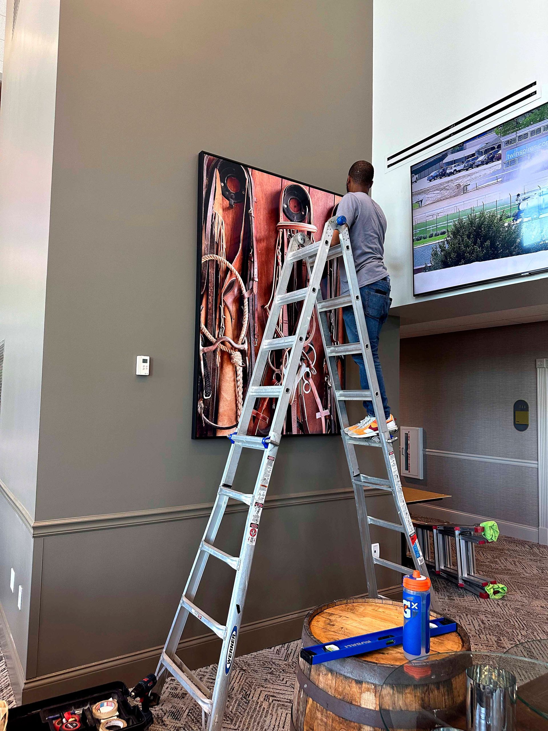 Person on ladder hanging art on wall. Modern interior with large canvas and large screen.