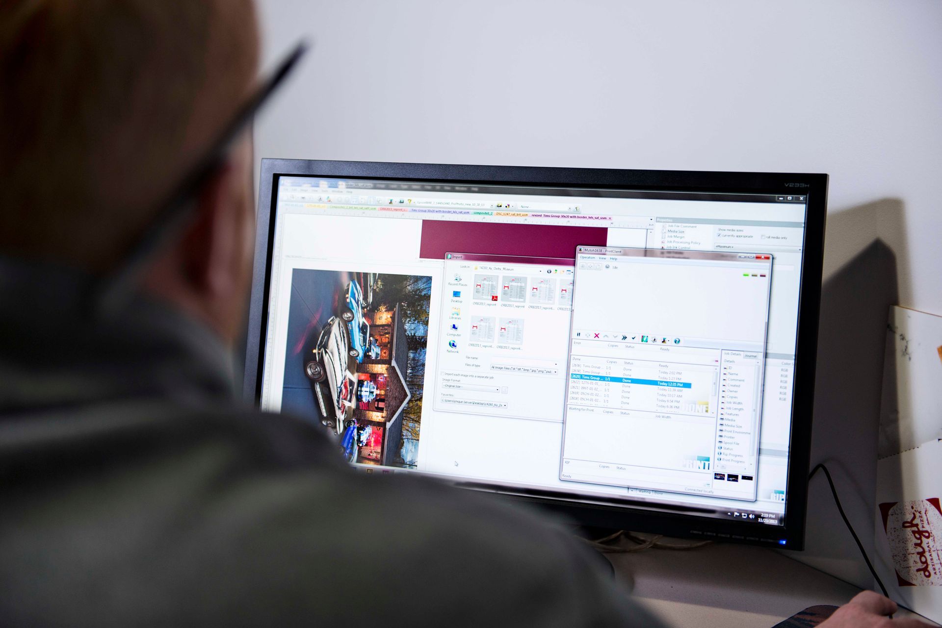 Person looking at a computer screen displaying multiple windows and a photo. White wall in background.