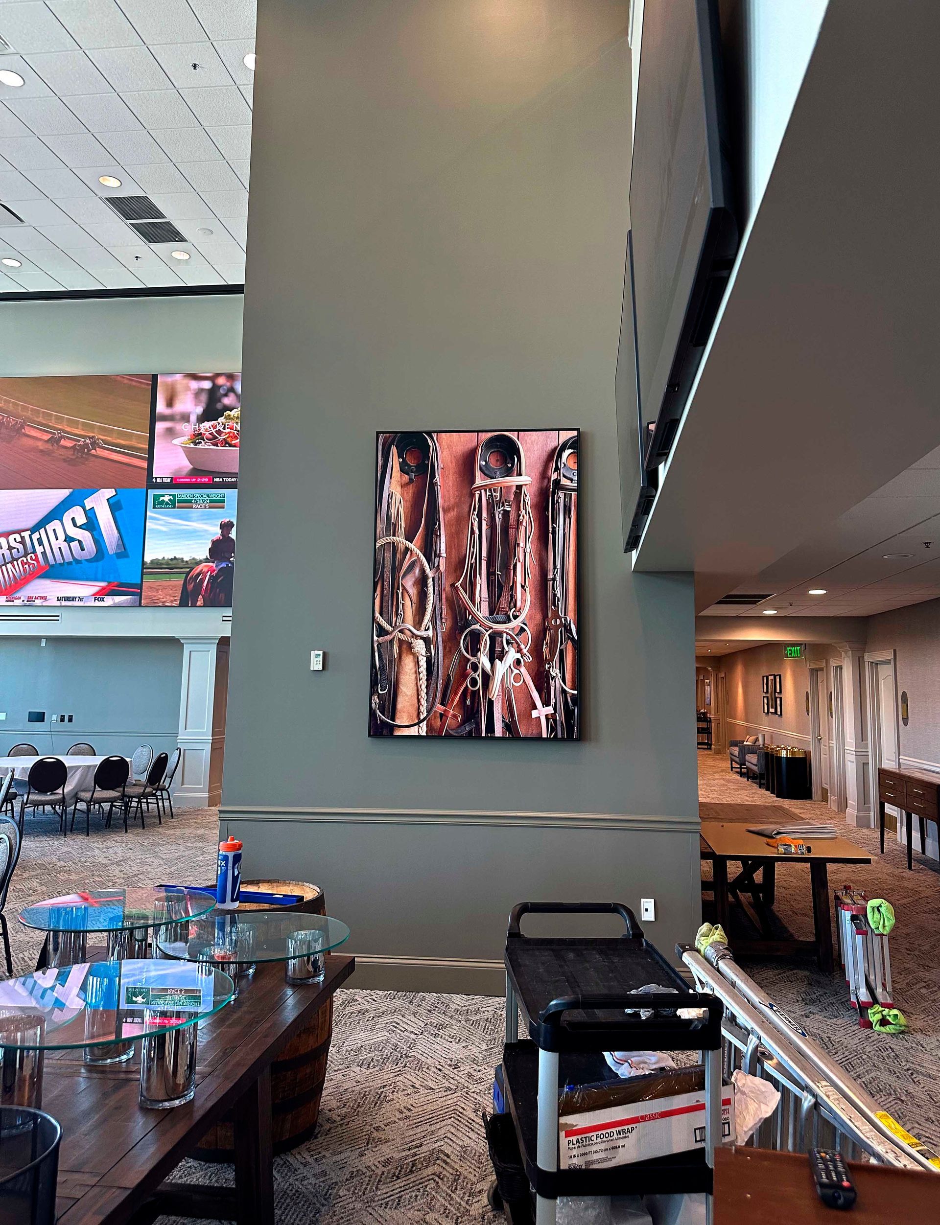 A large abstract art piece hangs on a green wall. A room with tables and screens is in the background.