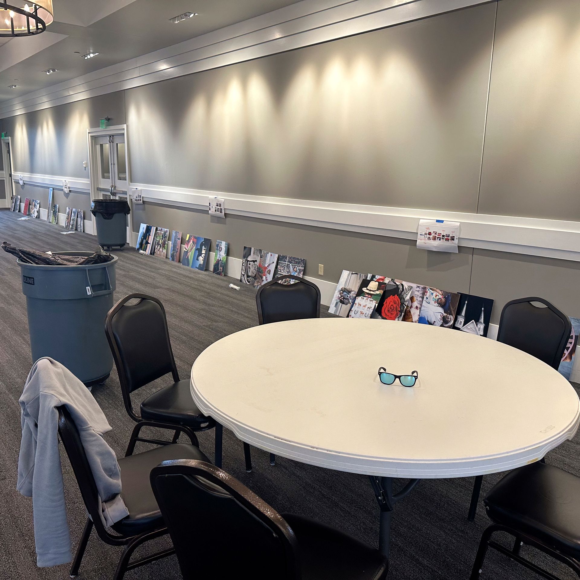 A round white table with chairs. Posters are against the wall. A hallway setting.