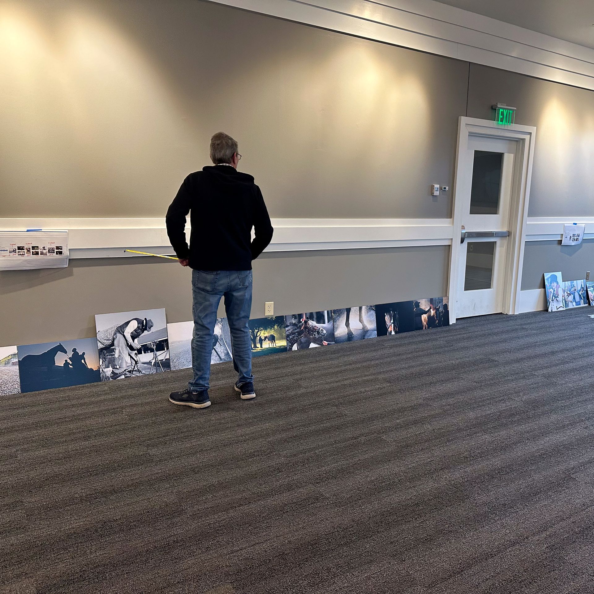 Person standing in front of a row of photos on a floor. They are in a room with neutral walls, carpet, and a door.