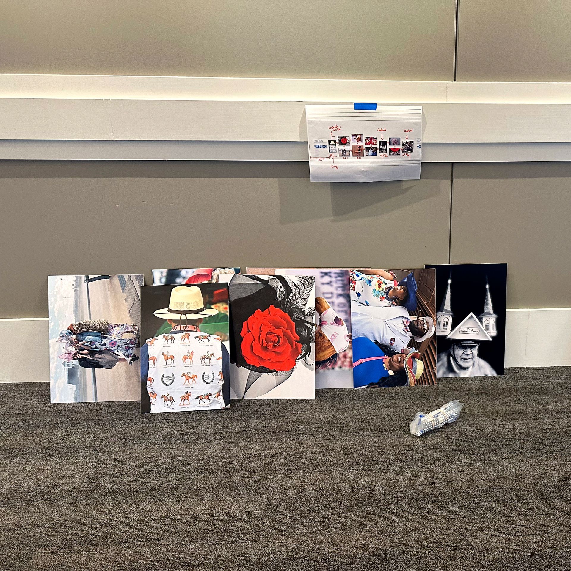 Row of art prints leaning against a wall, with a small print taped above them.