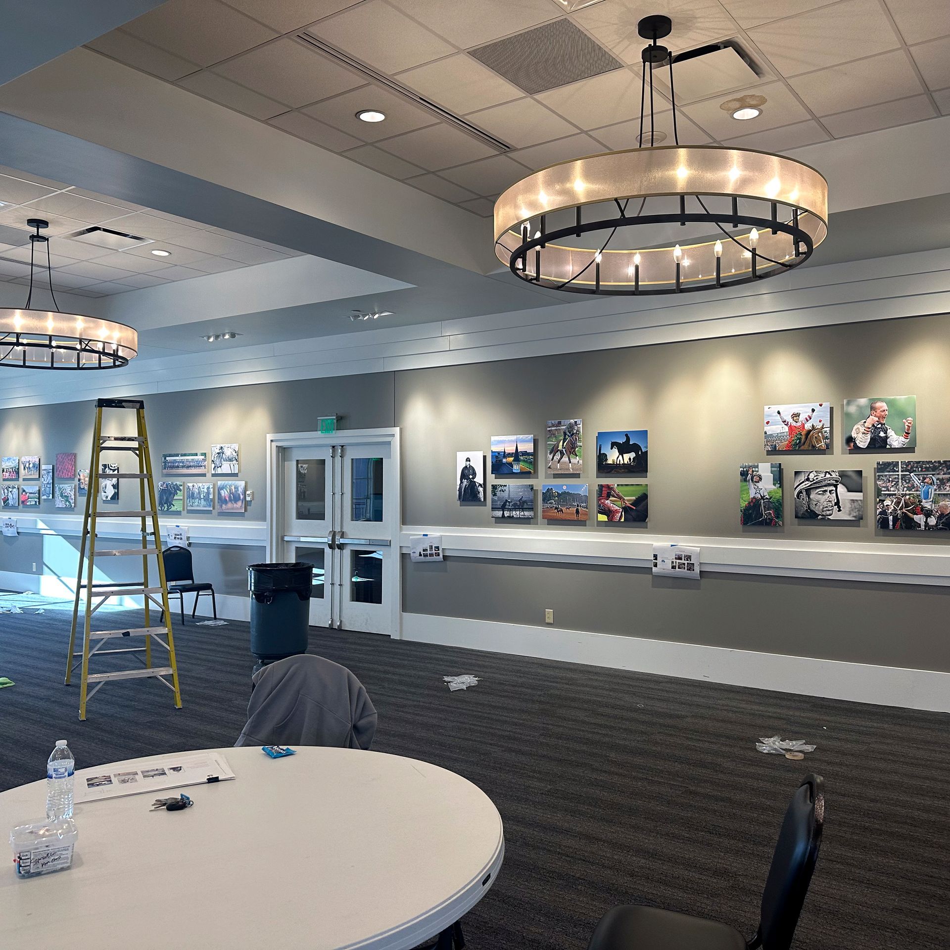 A room with artwork on the walls, tables, and a ladder.