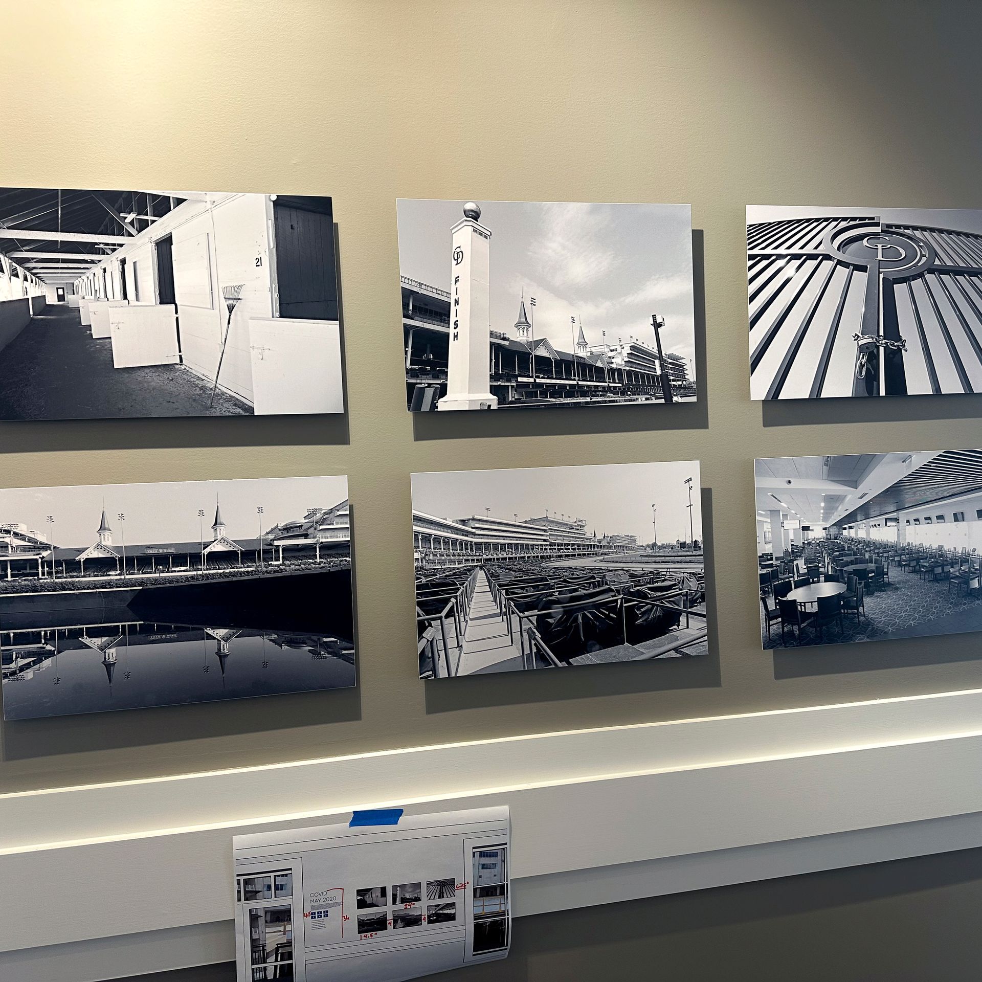 Six black and white framed photos on a wall. The photos depict waterfront scenes and buildings.