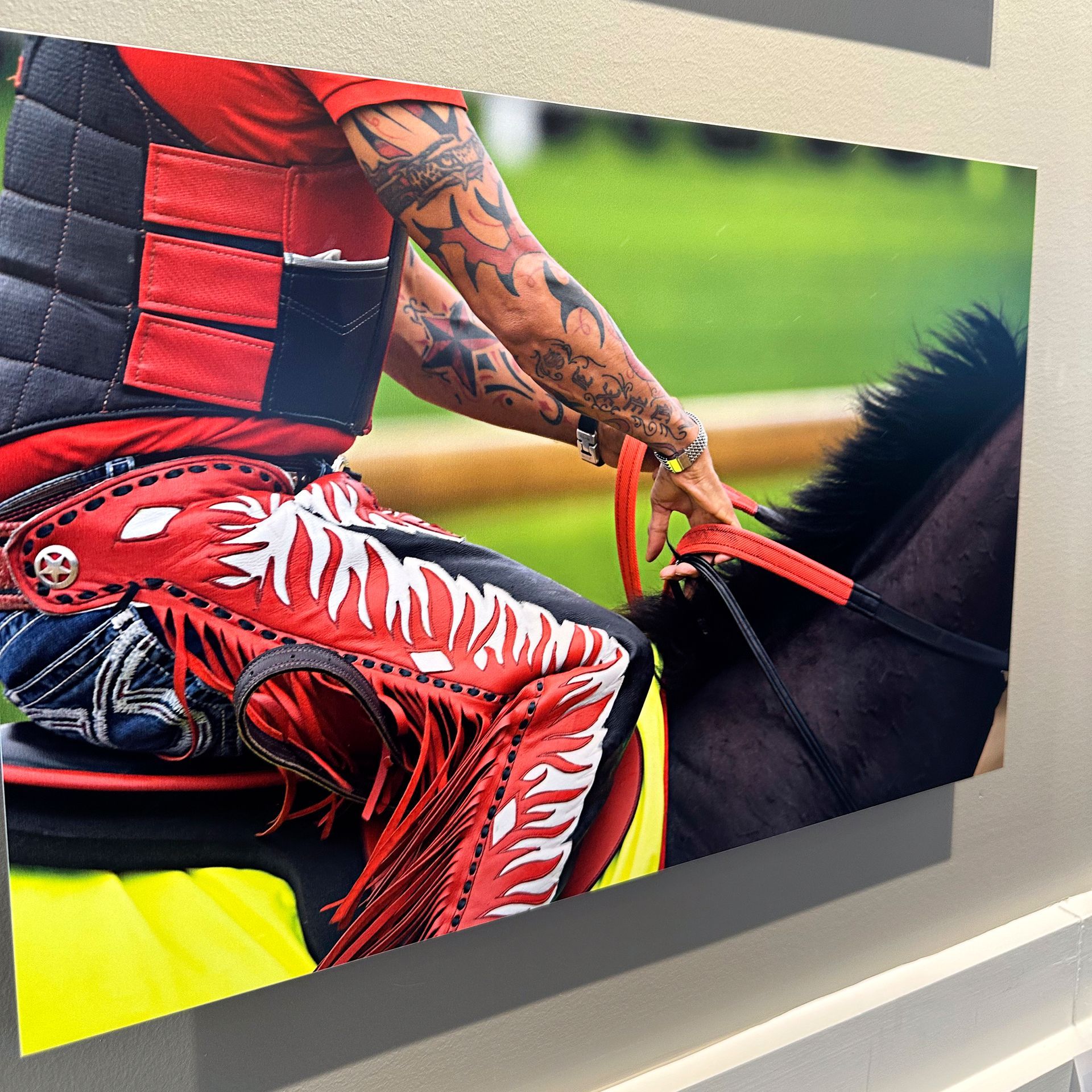 A person with arm tattoos on a horse, wearing red fringed chaps and vest.