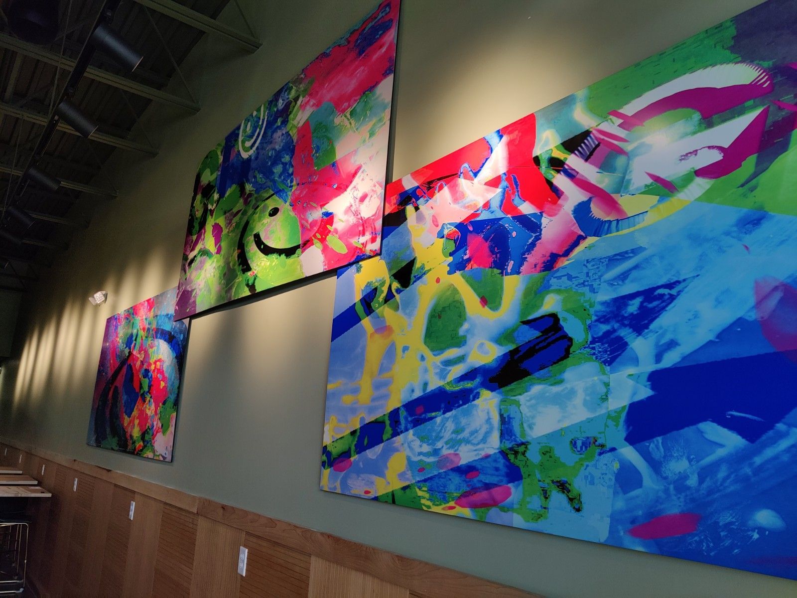 Abstract colorful paintings displayed on a wall in a dimly lit room.