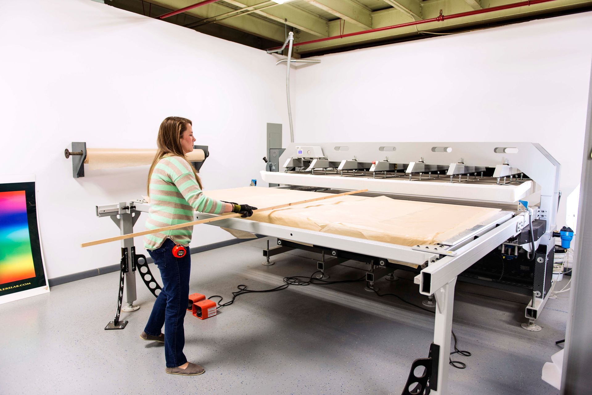Woman using a large industrial cutting machine in a workshop. A wooden panel is being measured.