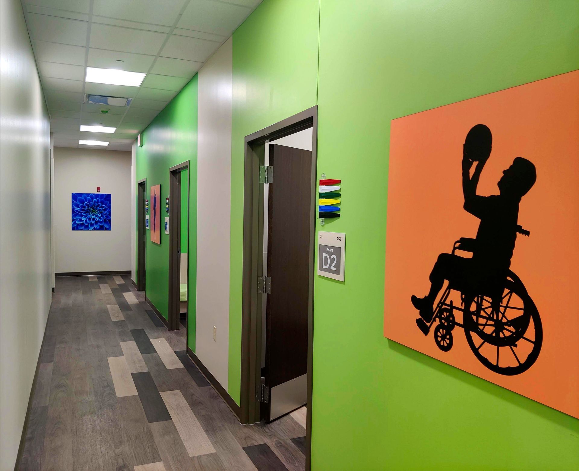 Hallway with green and white walls, wood-look flooring, and art. Silhouette of person in wheelchair playing basketball on orange wall.