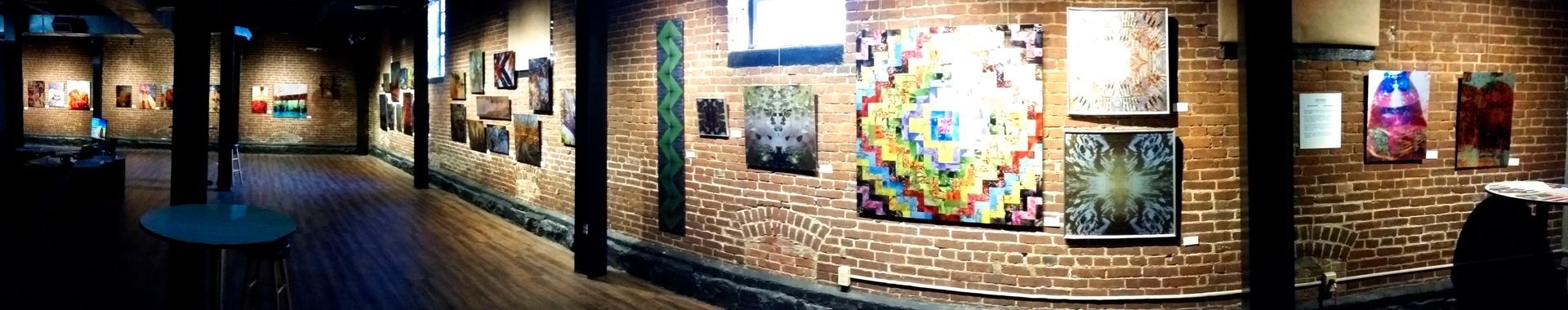 Art gallery interior with brick walls, artwork on display, and wooden floors.