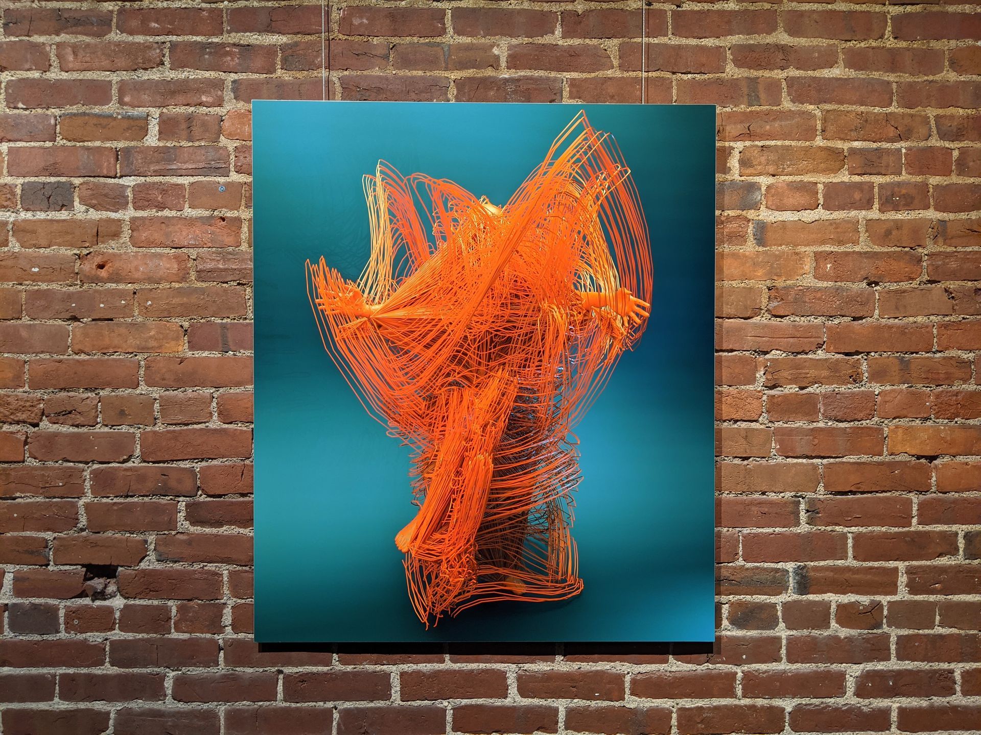 Artwork on a teal background. Orange abstract form against a brick wall.
