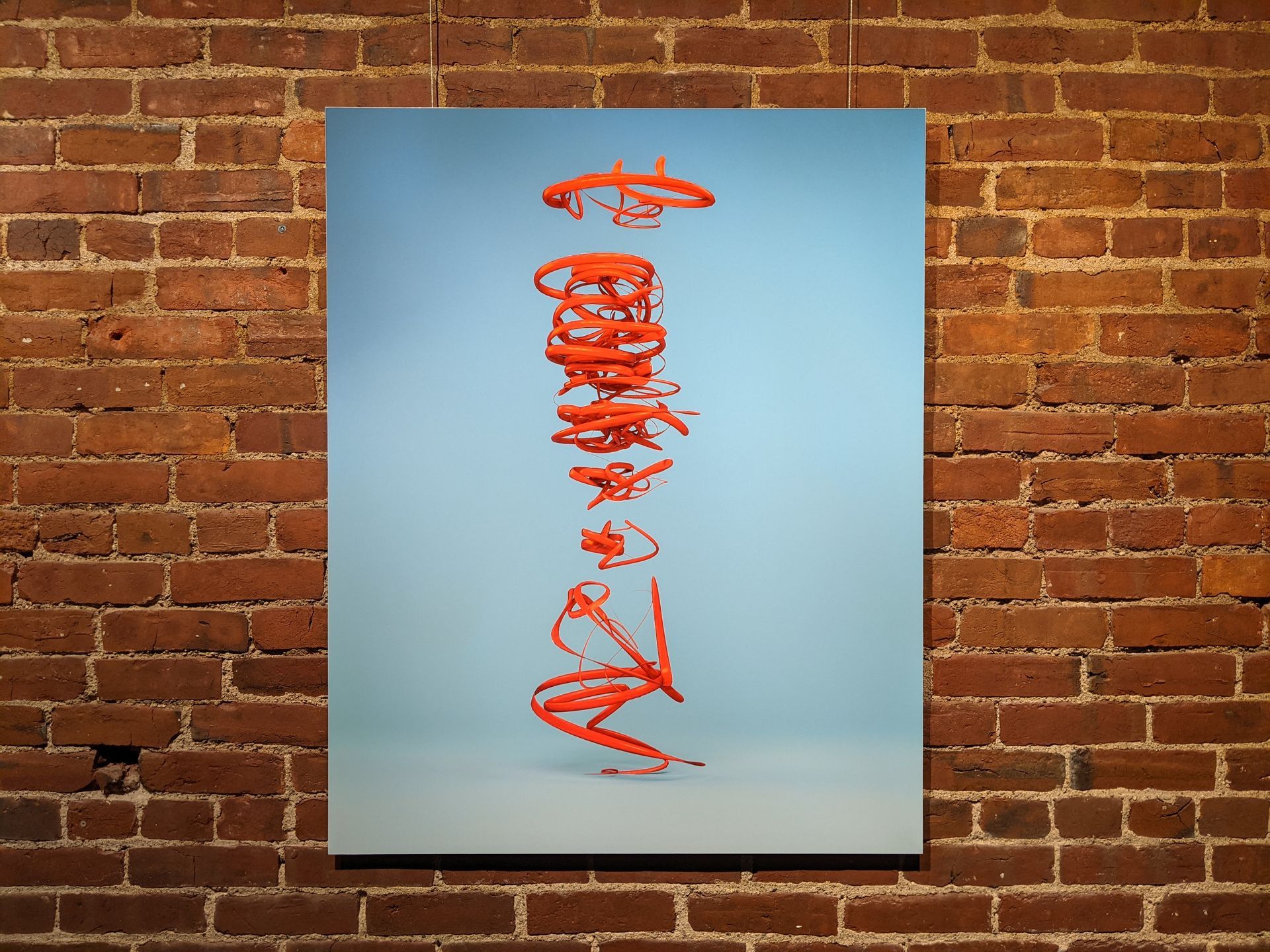 Artwork of a red, swirling sculpture against a light blue backdrop, hanging on a brick wall.