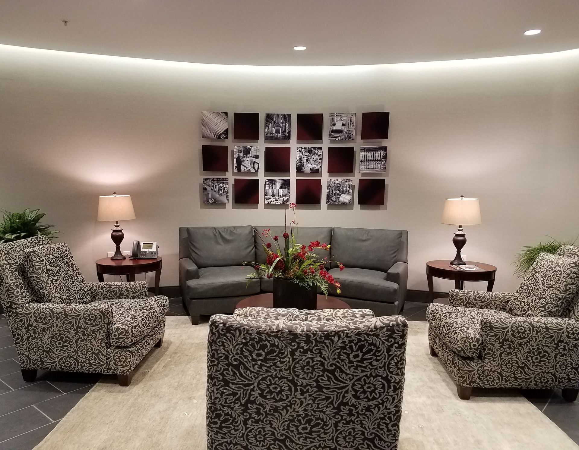 Lounge area with gray and patterned chairs, sofa, round tables, lamps, artwork, and a flower arrangement.