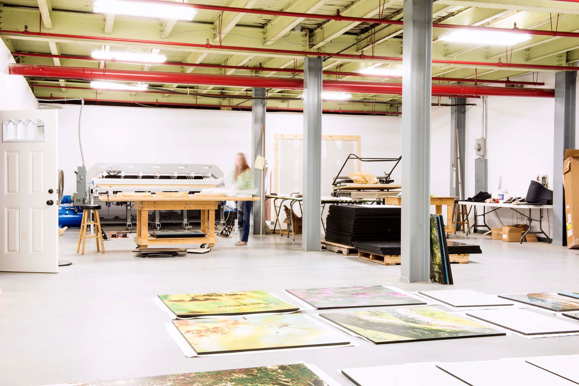 Large art studio with prints on the floor, equipment, and a person standing near a table.