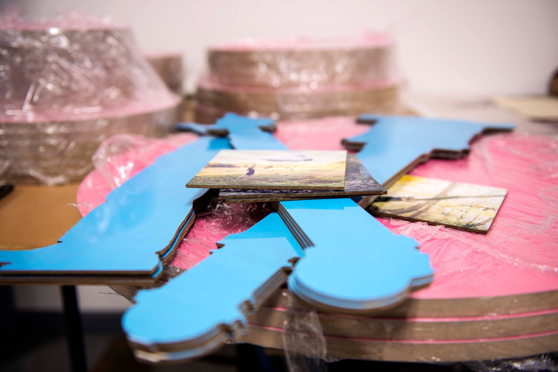 Blue state-shaped cutouts and picture fragments on pink-wrapped circular bases, likely for an art installation, inside a workshop.