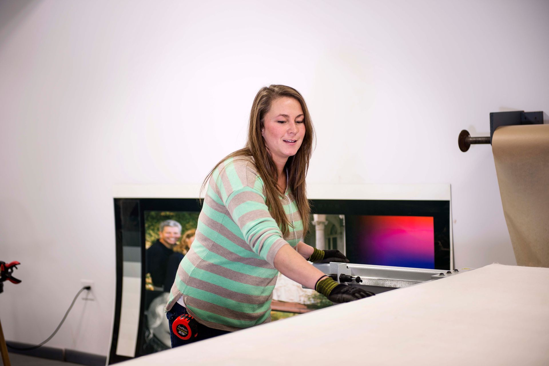 Woman in striped shirt working with large printer, smiling.