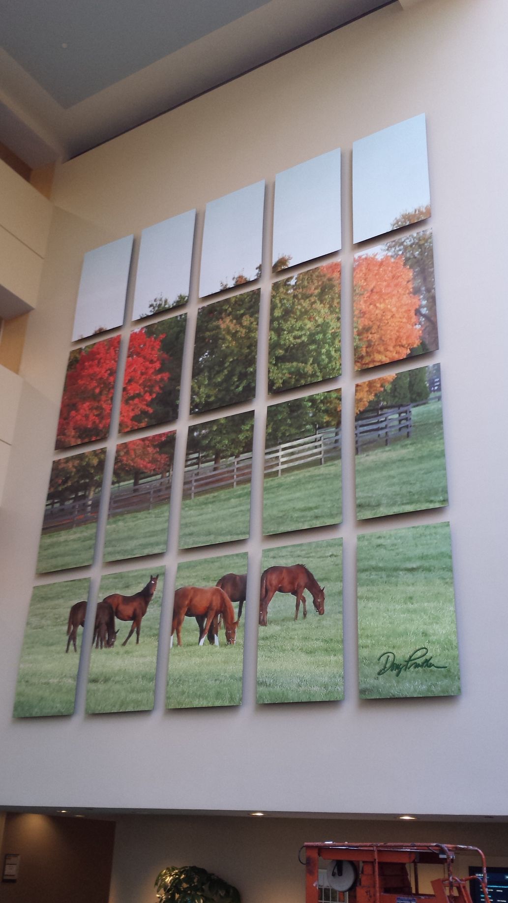Horses grazing in a grassy field with trees. Large wall art in a room.